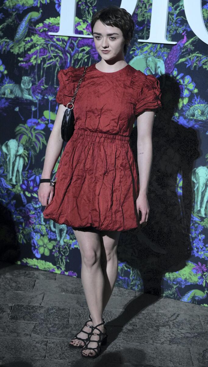 ممثلة Game of Thrones مايسي ويليامز ترتدي فستانًا أحمر مجعدًا بأكمام منفوخة.  اختارت زوجًا من الأحذية ذات الكعب الأسود وحقيبة سوداء متناسقة.
