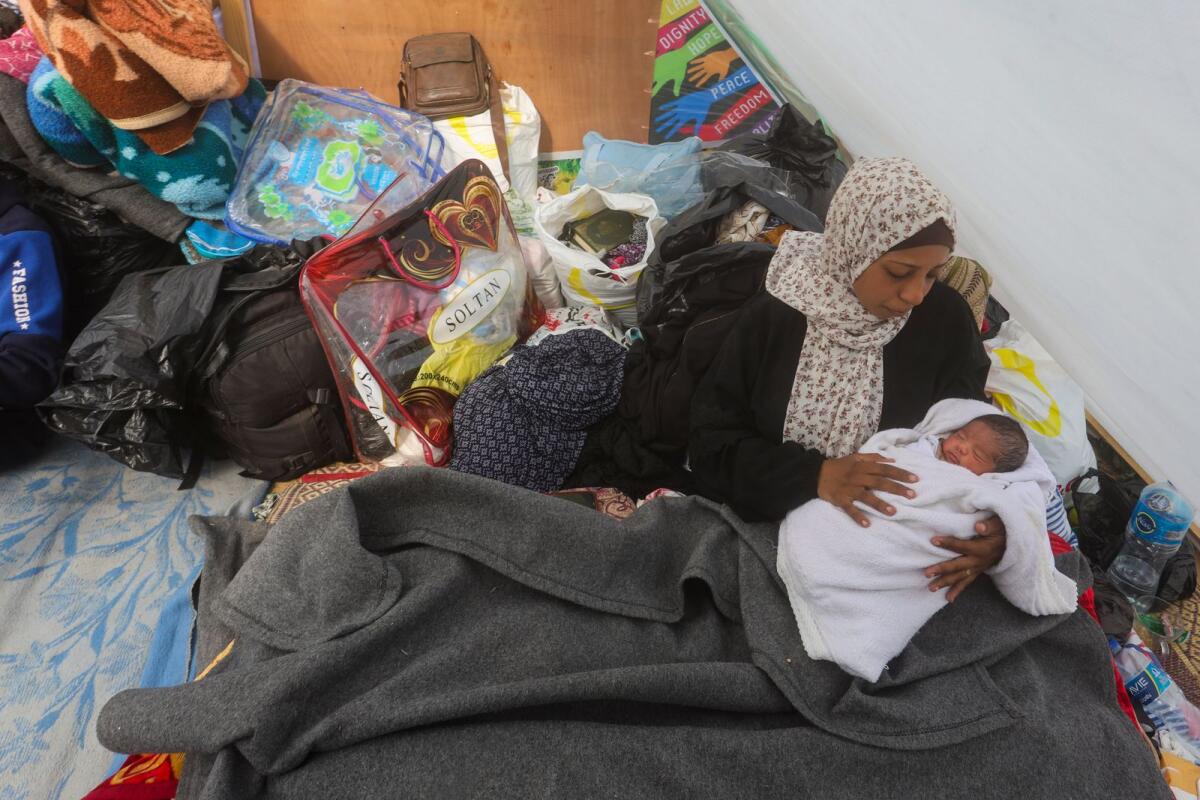 امرأة فلسطينية نزحت بسبب الهجوم الجوي والبري الإسرائيلي على قطاع غزة، تحمل طفلها في خيمة بالقرب من معبر كرم أبو سالم في رفح، 14 يناير، 2024. — AP