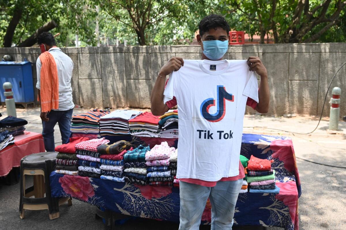 بائع متجول للملابس يقف لالتقاط صورة أمام كشكه وهو يرتدي قميصًا يحمل شعار تطبيق مشاركة الفيديو على وسائل التواصل الاجتماعي تيك توك في نيودلهي في 30 يونيو 2020. — AFP